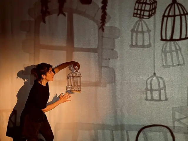 Femme avec une toile en fond et une cage à oiseau dans la main