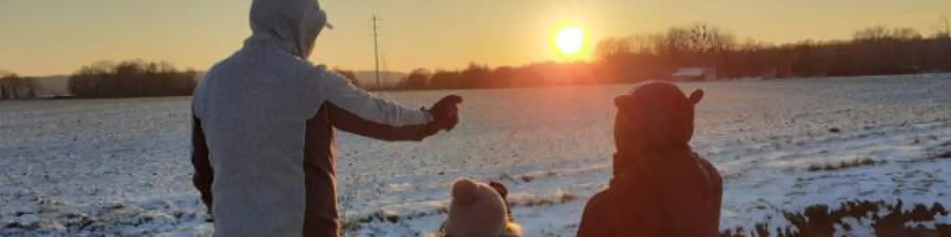 Un père et ses enfants en train de pointer le soleil en fin de journée avec un paysage enneigé