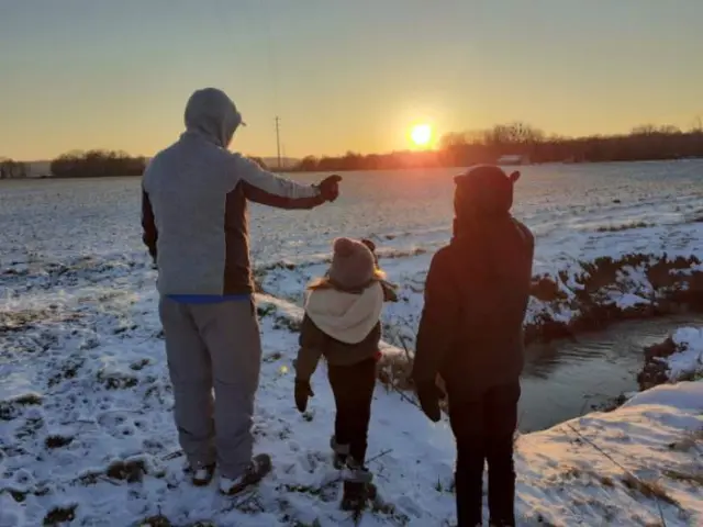 Un père et ses enfants en train de pointer le soleil en fin de journée avec un paysage enneigé